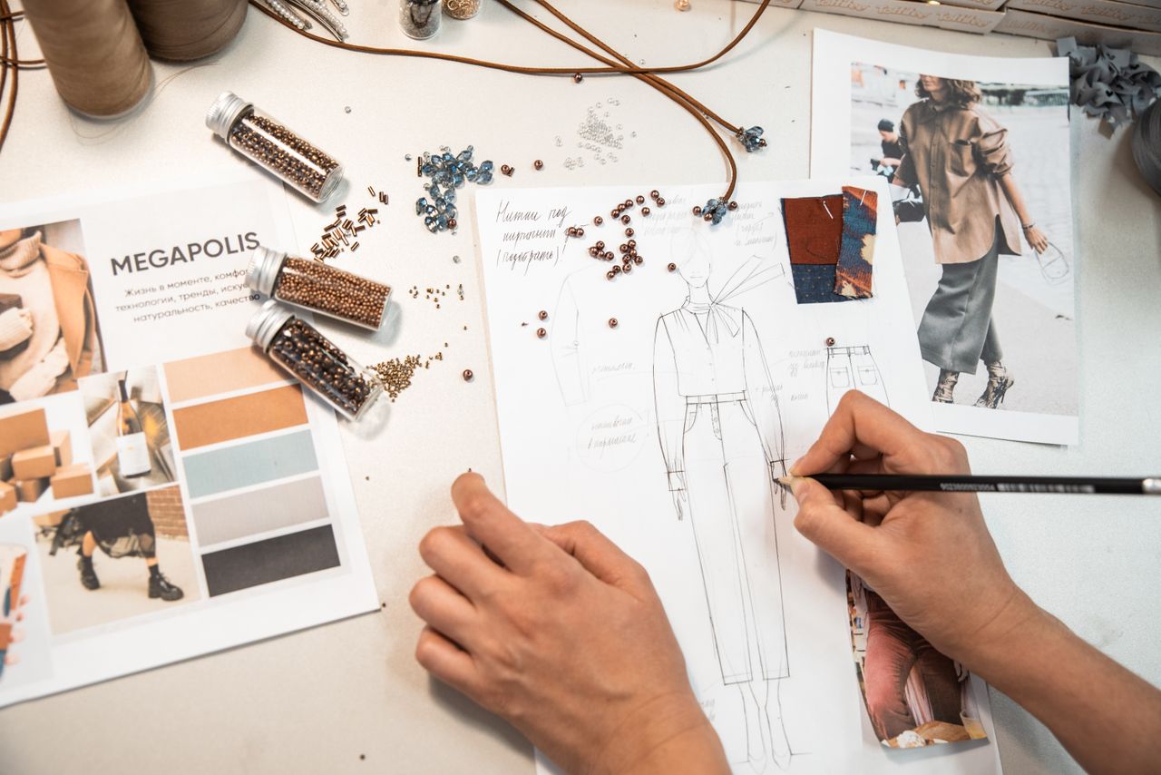 about-us Fashion designer sketching in a workspace with materials and mood boards.